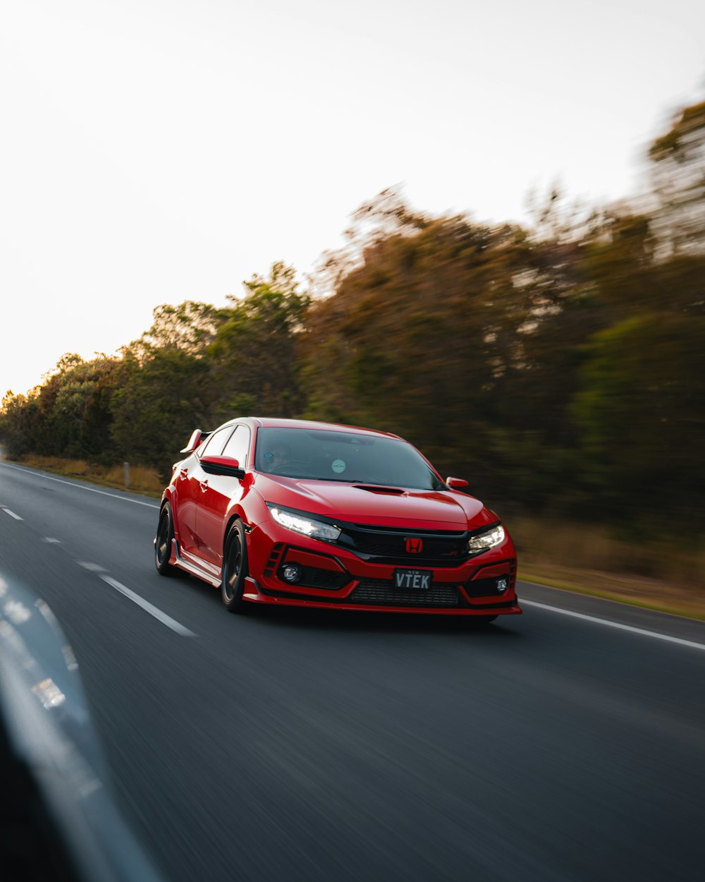 a red car driving down a road next to trees