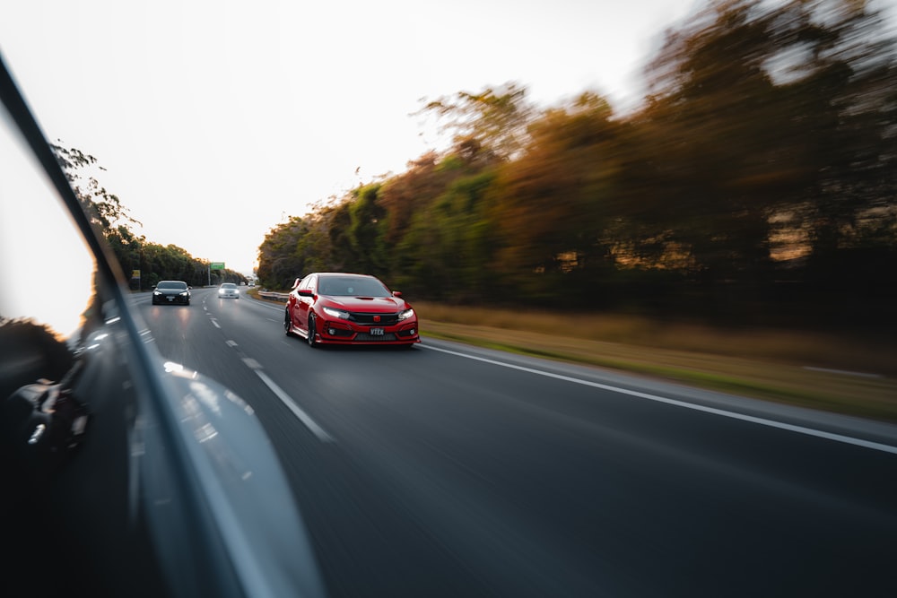 a red car driving down a road next to a forest