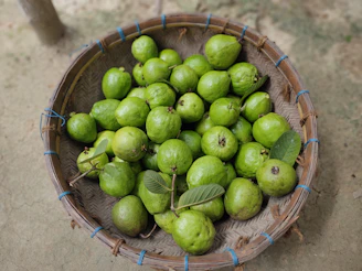 A rustic basket filled with assorted pitahayas and green leaves on a wooden table.