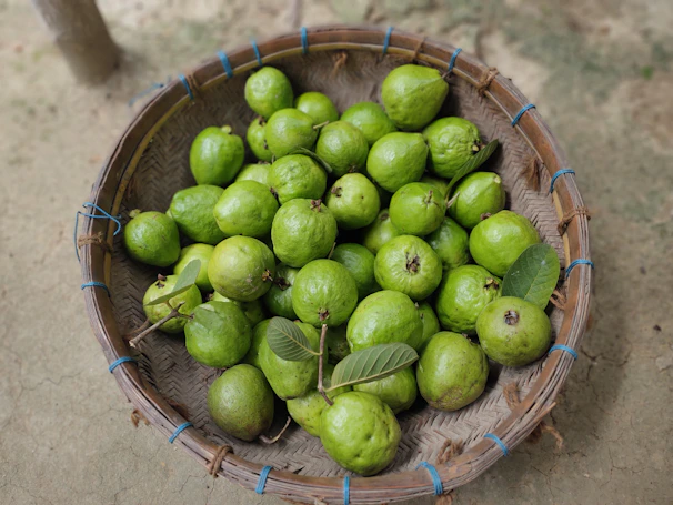 A rustic basket filled with assorted pitahayas and green leaves on a wooden table.