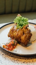 A plated dish consisting of a piece of crispy fried chicken garnished with lettuce, served alongside a mound of white rice and a side of colorful mixed vegetables or salad.