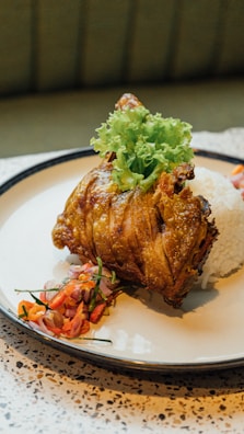 A plated dish consisting of a piece of crispy fried chicken garnished with lettuce, served alongside a mound of white rice and a side of colorful mixed vegetables or salad.