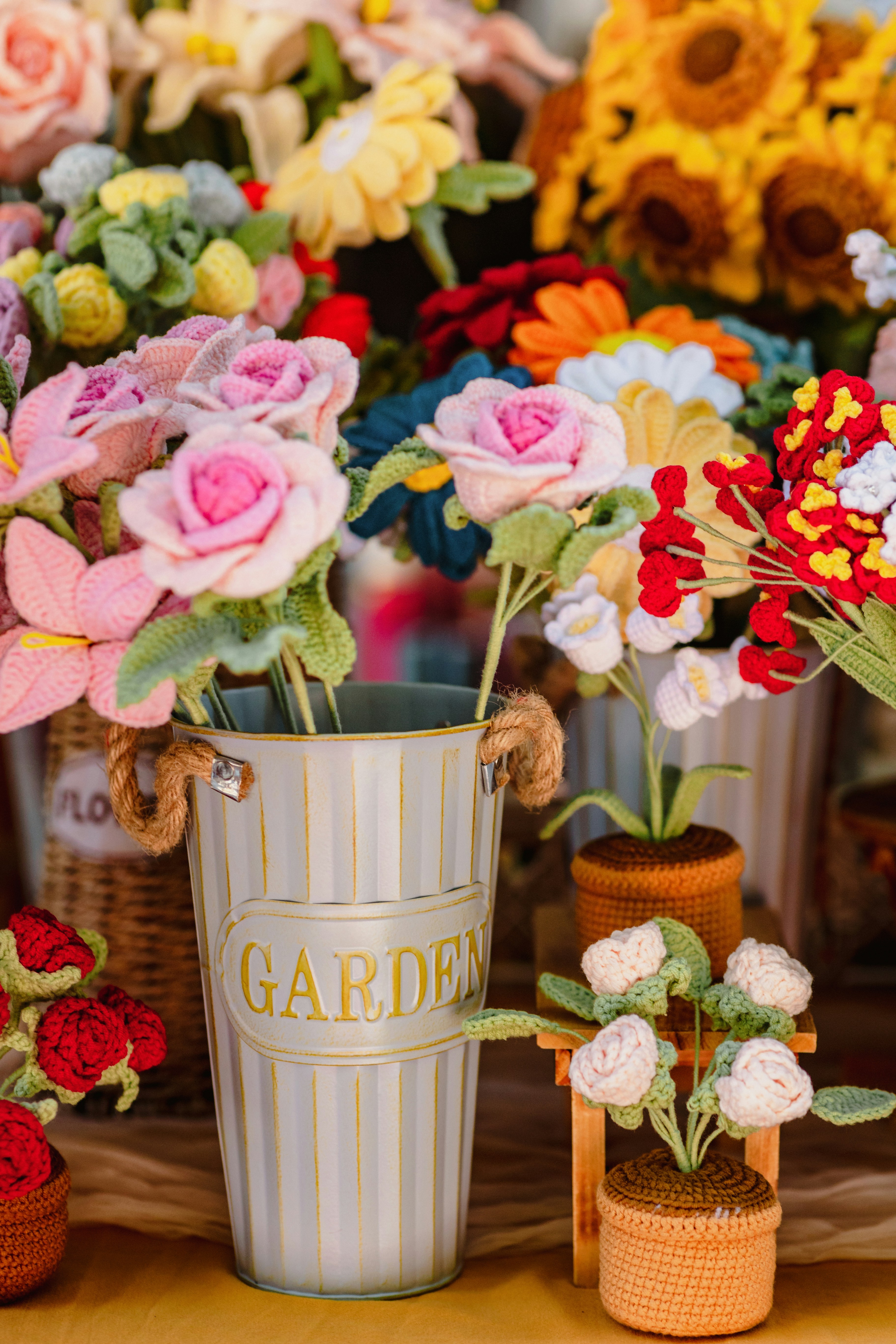 Colorful crocheted flowers displayed in a garden bucket and woven pots.