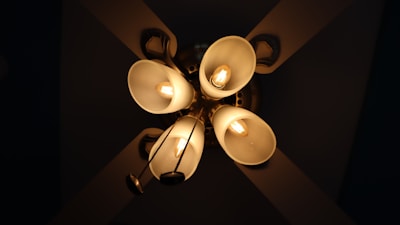 Five downward-facing light bulbs encased in frosted, bell-shaped glass holders form an elegant chandelier. The bulbs radiate a warm, golden glow, creating a cozy ambiance. The fixture's metal arms and hub are visible, providing structural support.