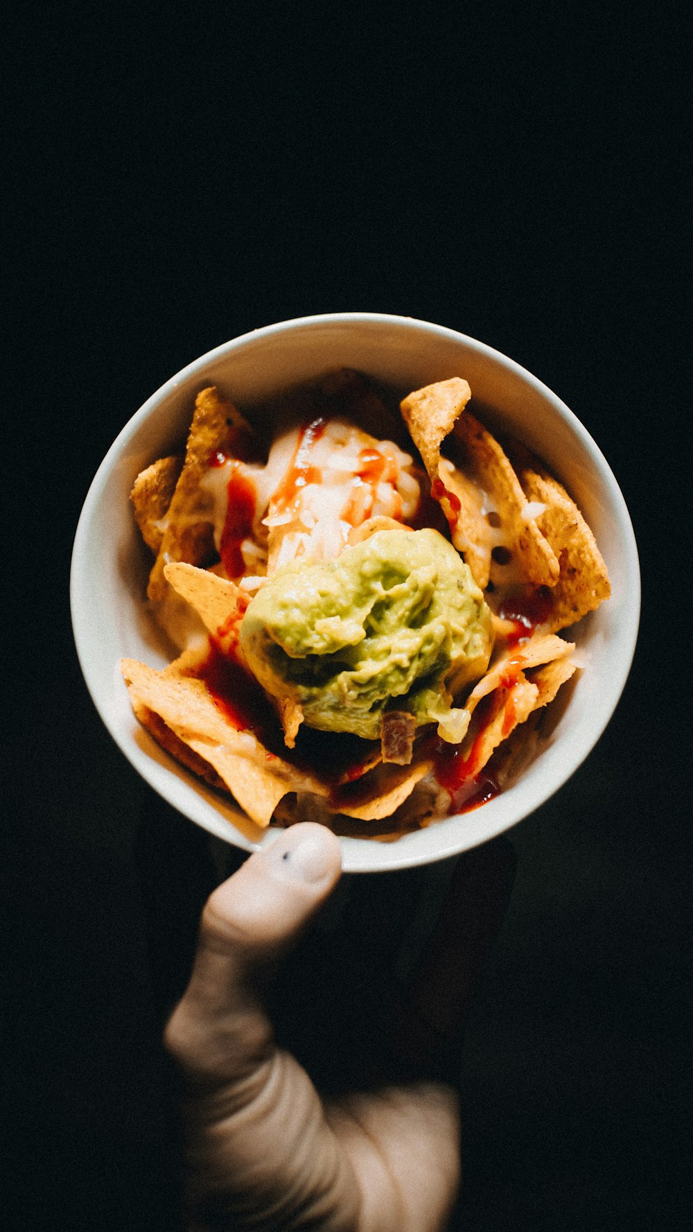 a person holding a bowl of nachos with guacamole
