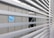 Slatted blinds partially obscure the view of an industrial structure with metal casing. A blue circular sign with 'BAC' is visible. The environment appears to be an industrial setting with elements of metal and machinery.