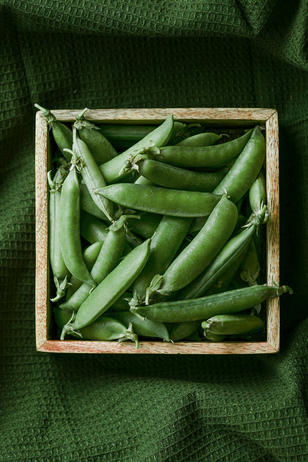 a wooden box filled with green beans on a green cloth