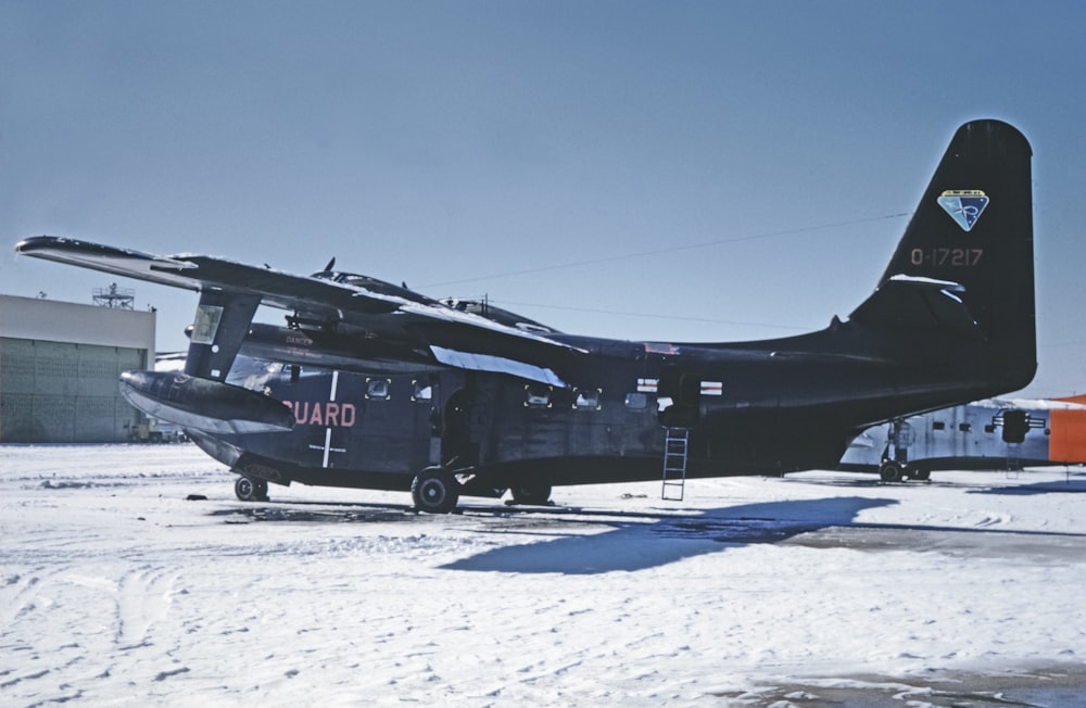 a black airplane sitting on top of a snow covered field
