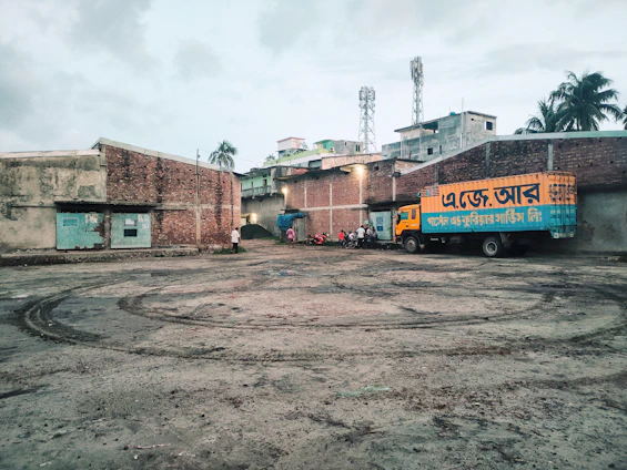 A fleet of diverse trucks parked at a bustling logistics yard under a bright sky in Bangladesh.