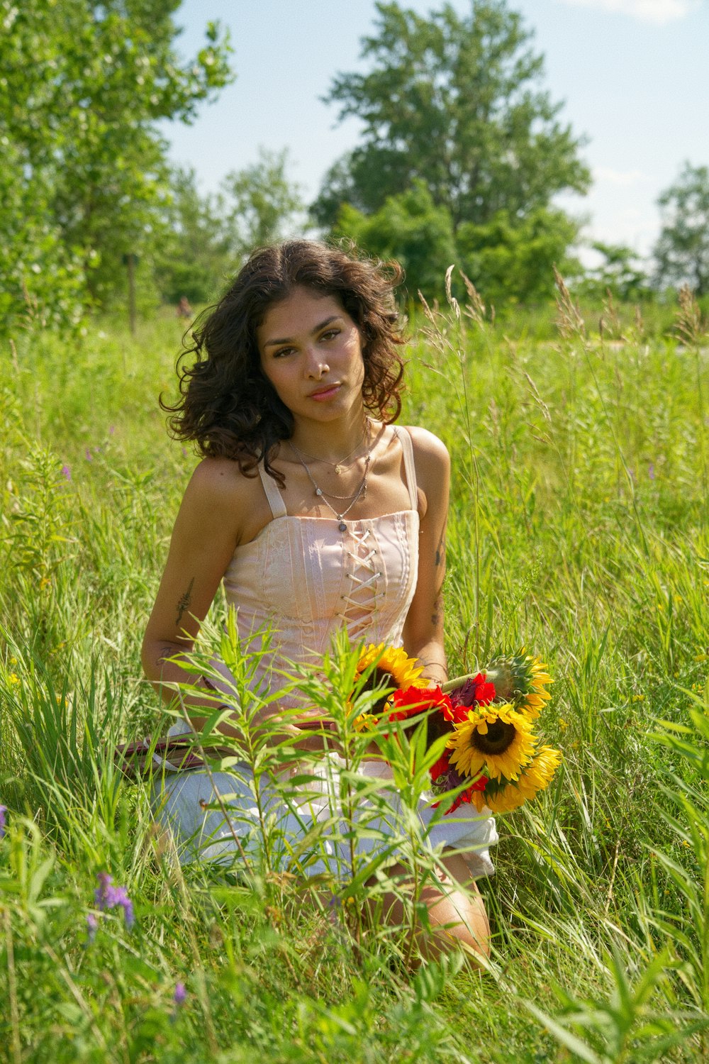 a woman sitting in a field holding a bouquet of flowers