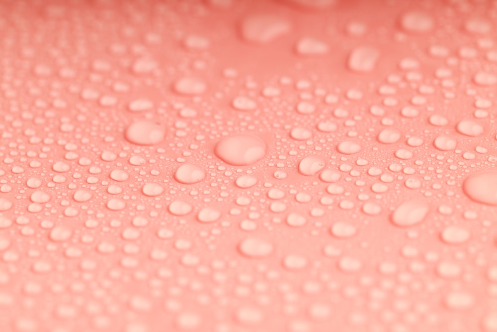 a close up of water droplets on a pink surface