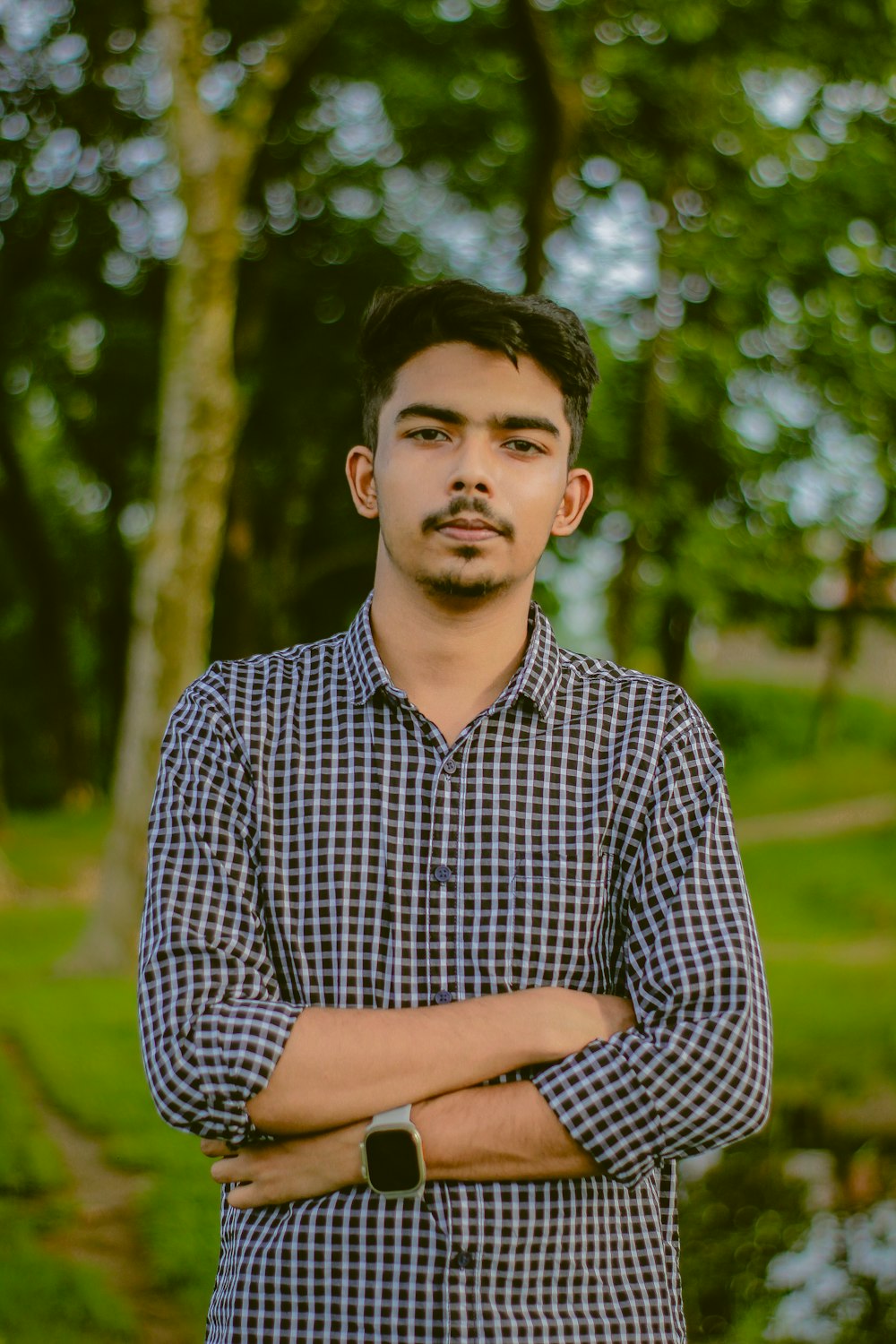 a man standing with his arms crossed in a park