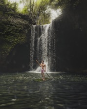 a man standing on a surfboard in front of a waterfall