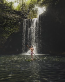 a man standing on a surfboard in front of a waterfall