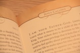A close-up of an open book displaying text with the heading 'JESUS CALLING'. The text appears to be a religious or spiritual message, with focus on phrases like 'I AM YOUR FATHER-GOD' and discussion of devotion and spiritual duties.