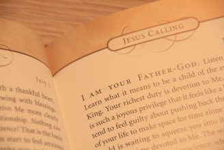 A close-up of an open book displaying text with the heading 'JESUS CALLING'. The text appears to be a religious or spiritual message, with focus on phrases like 'I AM YOUR FATHER-GOD' and discussion of devotion and spiritual duties.
