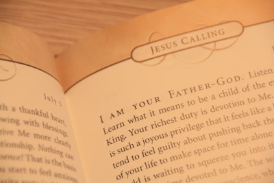 A close-up of an open book displaying text with the heading 'JESUS CALLING'. The text appears to be a religious or spiritual message, with focus on phrases like 'I AM YOUR FATHER-GOD' and discussion of devotion and spiritual duties.