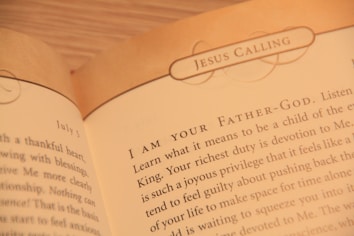 A close-up of an open book displaying text with the heading 'JESUS CALLING'. The text appears to be a religious or spiritual message, with focus on phrases like 'I AM YOUR FATHER-GOD' and discussion of devotion and spiritual duties.