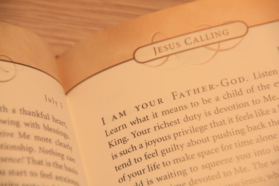 A close-up of an open book displaying text with the heading 'JESUS CALLING'. The text appears to be a religious or spiritual message, with focus on phrases like 'I AM YOUR FATHER-GOD' and discussion of devotion and spiritual duties.