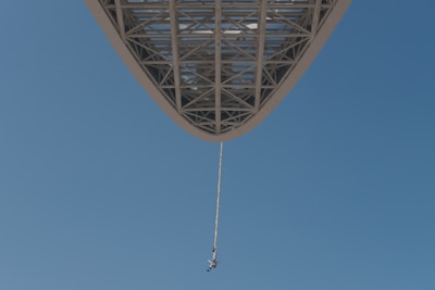 Close-up of a bungee jumper launching off a vibrant red crane against a clear blue sky.