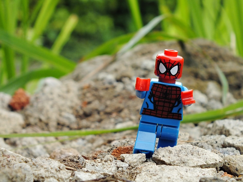 a lego spider man standing on some rocks
