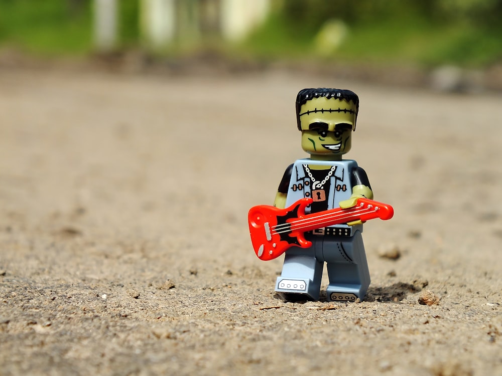 a lego figure holding a red guitar in the sand