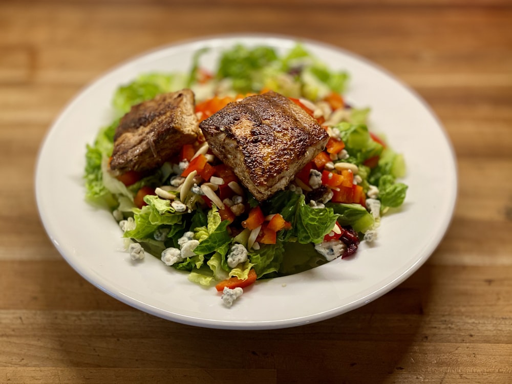 a white plate topped with a salad covered in meat