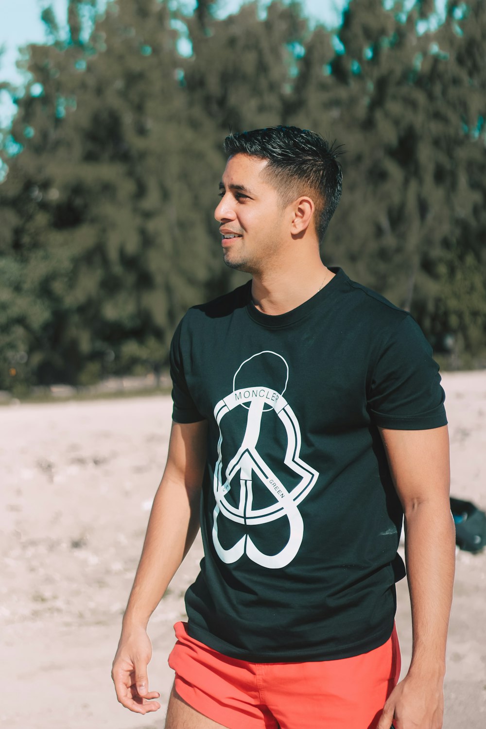 a man standing on a beach wearing a black shirt with a peace sign on it