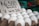 A carton of white eggs is prominently displayed with a handwritten sign indicating the price and quantity. The background features a blurred market setting with various produce.