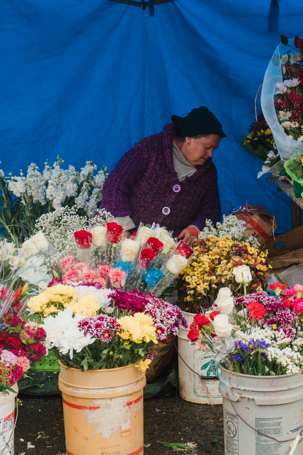 a woman arranging flowers in buckets in front of a blue tarp