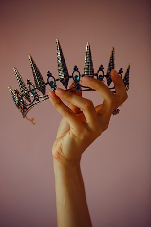 Close-up of elegant hands holding a sparkling quinceañera tiara against a soft pastel background.