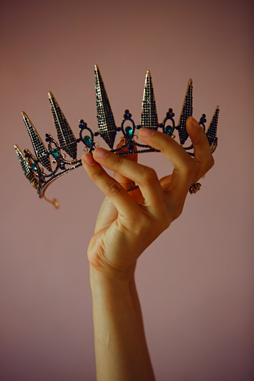 a hand holding a tiara in front of a pink background