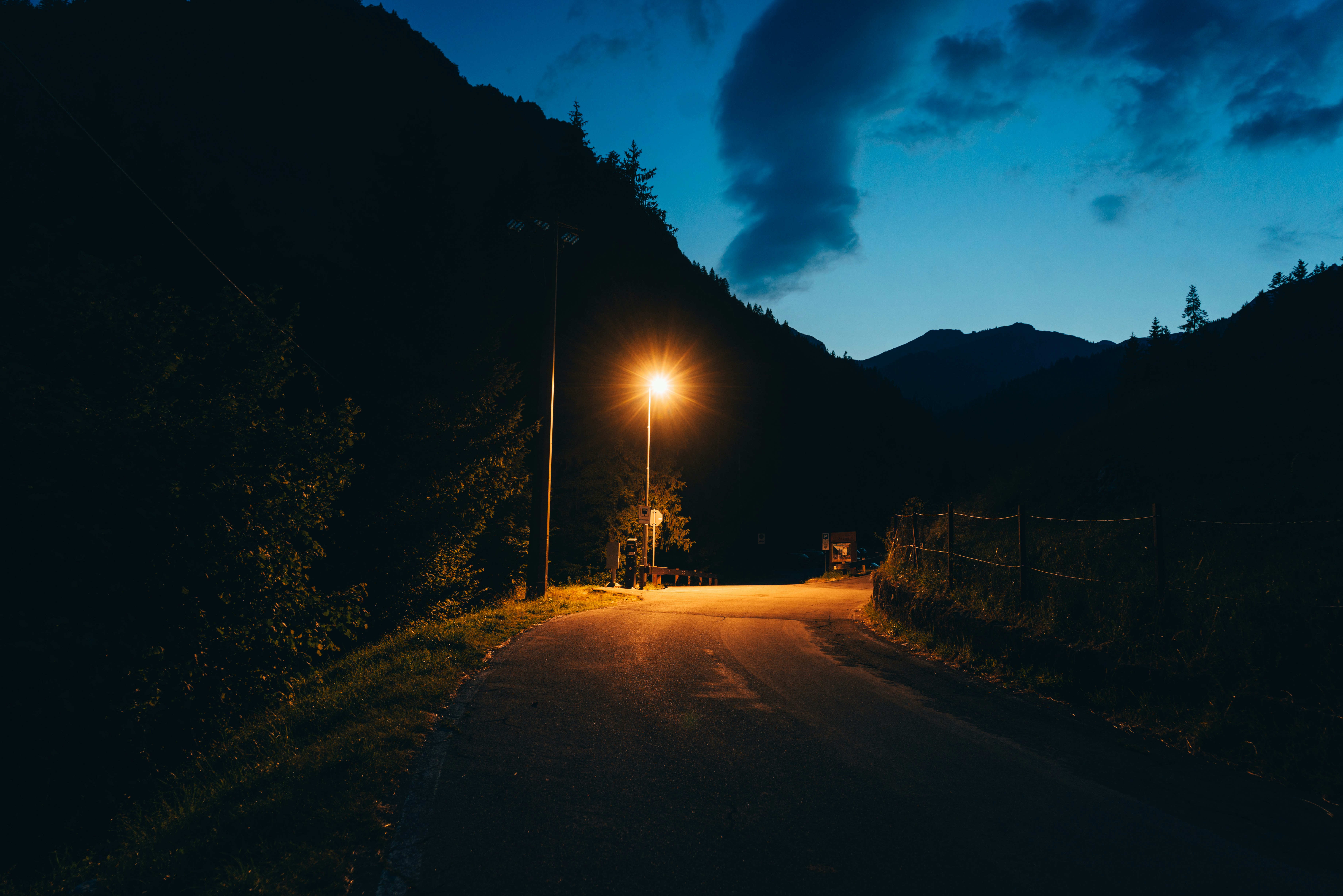 A dark, winding road in the mountains at night, with a faint light in the distance.