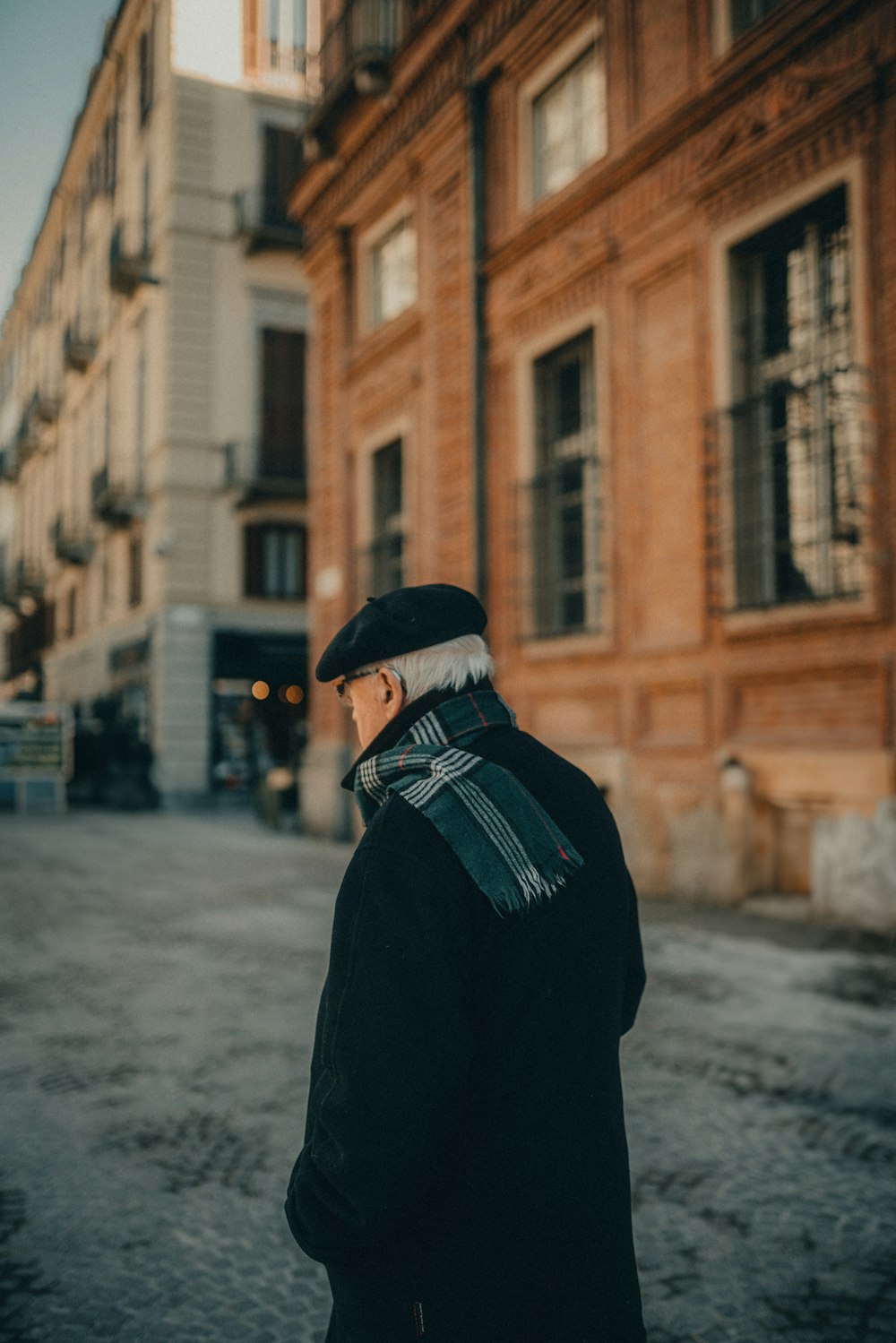 a man in a black coat and hat walking down a street