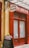 A storefront with vibrant red doors and window frames, featuring a traditional butcher shop sign that reads 'Boucherie Charcuterie' in French. A chalkboard menu is displayed outside, listing various offerings. The atmosphere suggests a quaint, classic European shop.