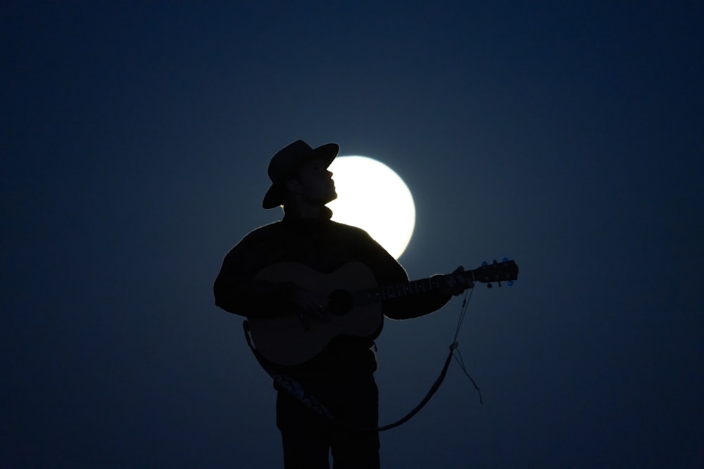 a man playing a guitar in front of a full moon