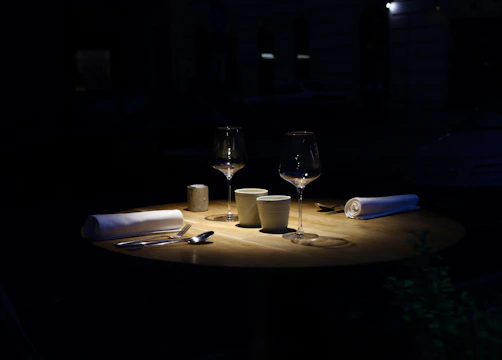 A dimly lit dinner table set for two, shadows hinting at tension.