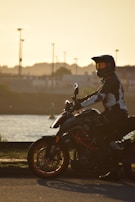 A person wearing a rugged leather jacket sitting on a motorcycle at sunset.