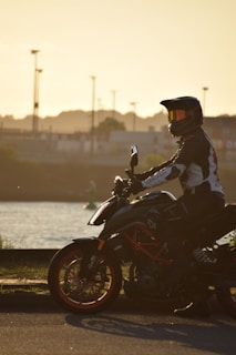A person wearing a rugged leather jacket sitting on a motorcycle at sunset.