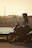 Motorcyclist wearing leather gear and holding a handmade leather bag, sunset background