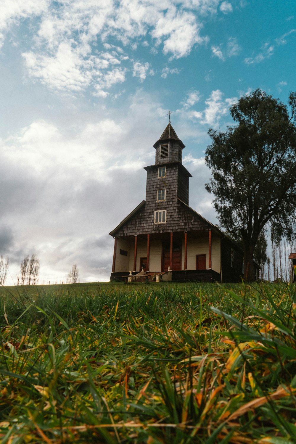 a small church with a steeple on a grassy hill