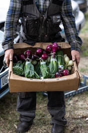 a man holding a cardboard box full of vegetables
