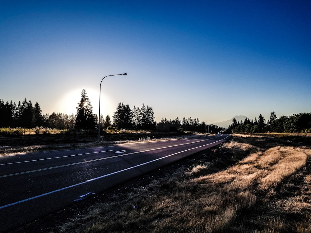 the sun is setting over a road with a grassy field