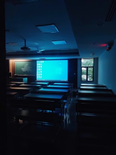 a dark room with tables and chairs and a projector screen