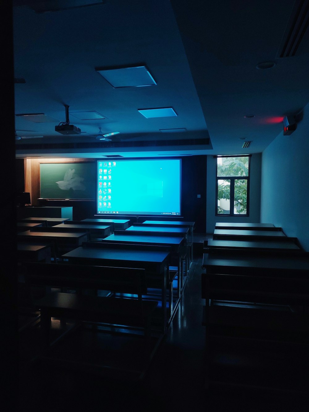 a dark room with tables and chairs and a projector screen