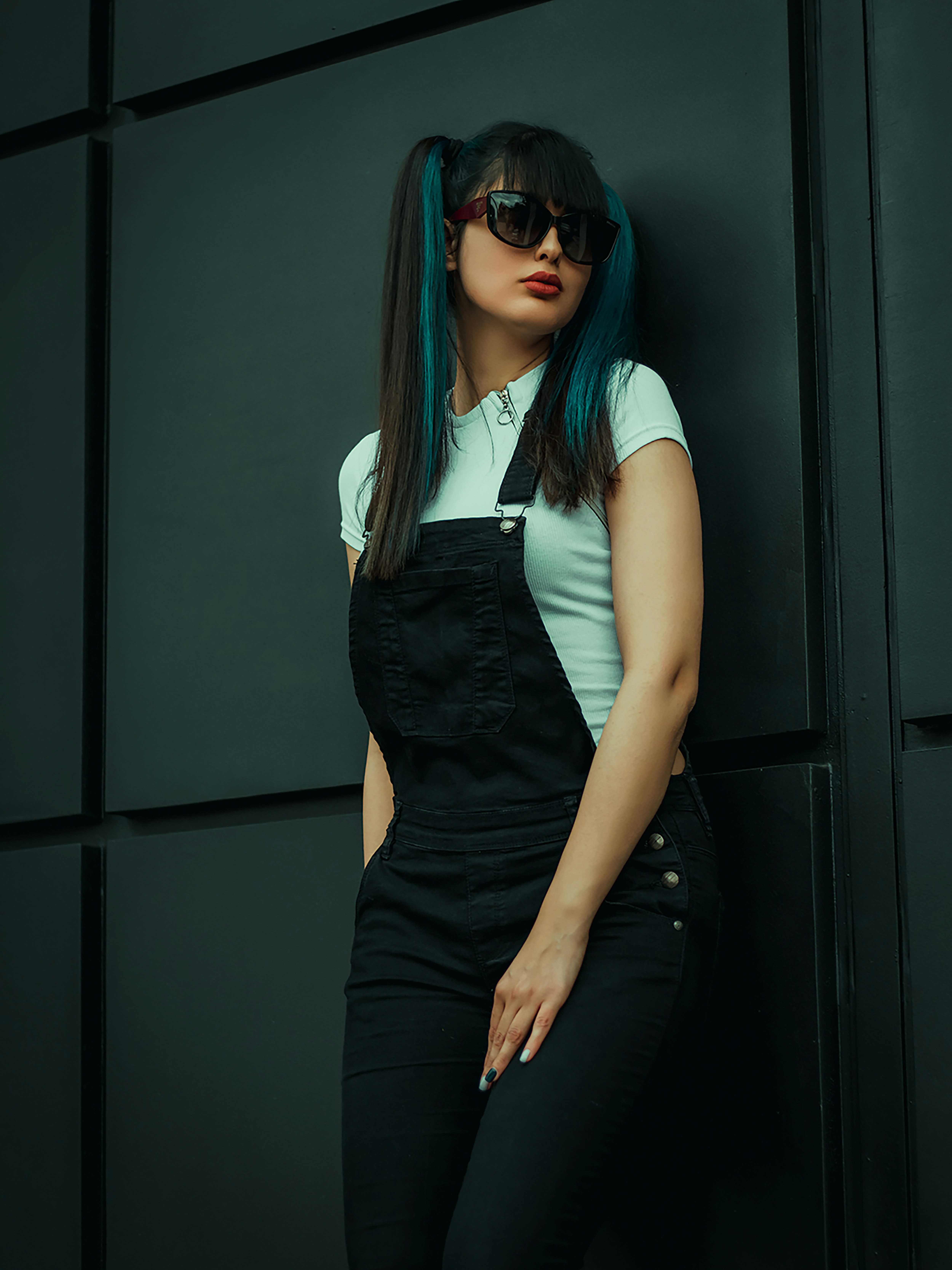 a woman with blue hair and sunglasses leaning against a wall