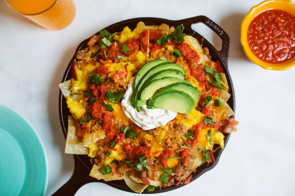 a skillet filled with nachos, salsa, guacamole and
