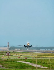 Airplane taking off with a large warehouse in the background.