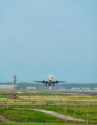 An airplane taking off over green fields with bright morning light.