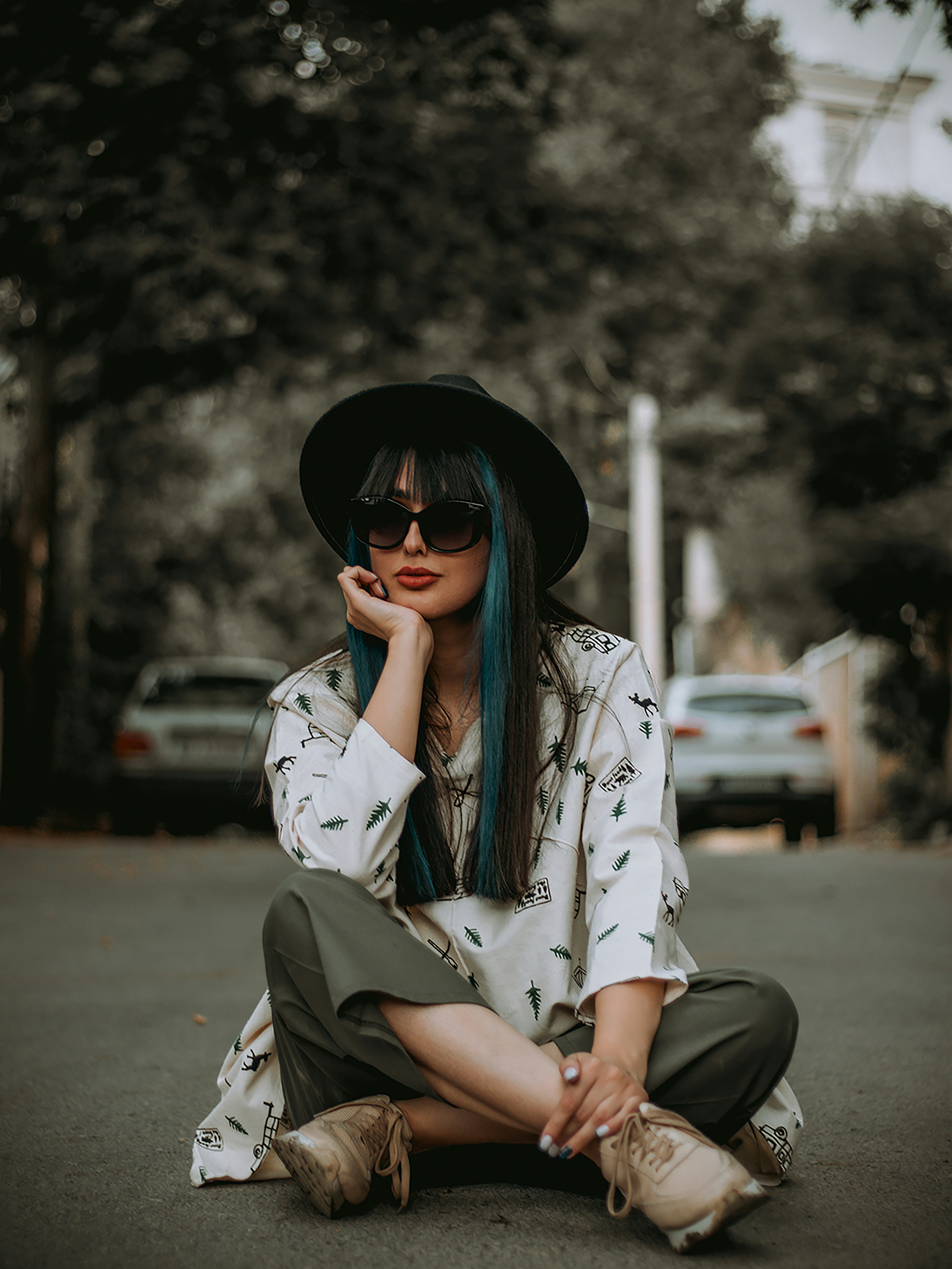 a woman sitting on the ground wearing a hat and sunglasses